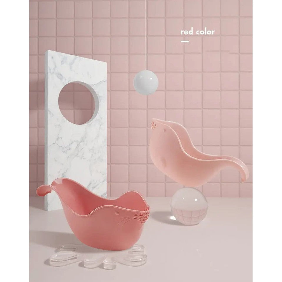 Two BC Babycare Shower Rinse Cups in pink, bird-shaped bath cups with curved beaks scooping water beside a marble panel.