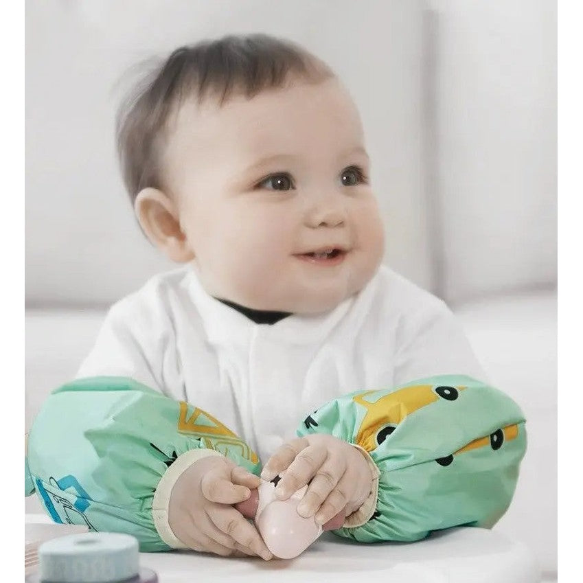 BC Babycare Waterproof Arm Sleeve, green printed design, worn on baby's arms as they grip a pink toy.