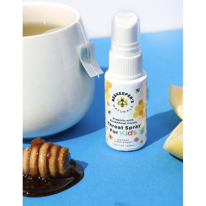 Beekeeper's Naturals Propolis Honey Throat Spray for Kids, 30 ml, spray bottle beside honey dipper on blue background