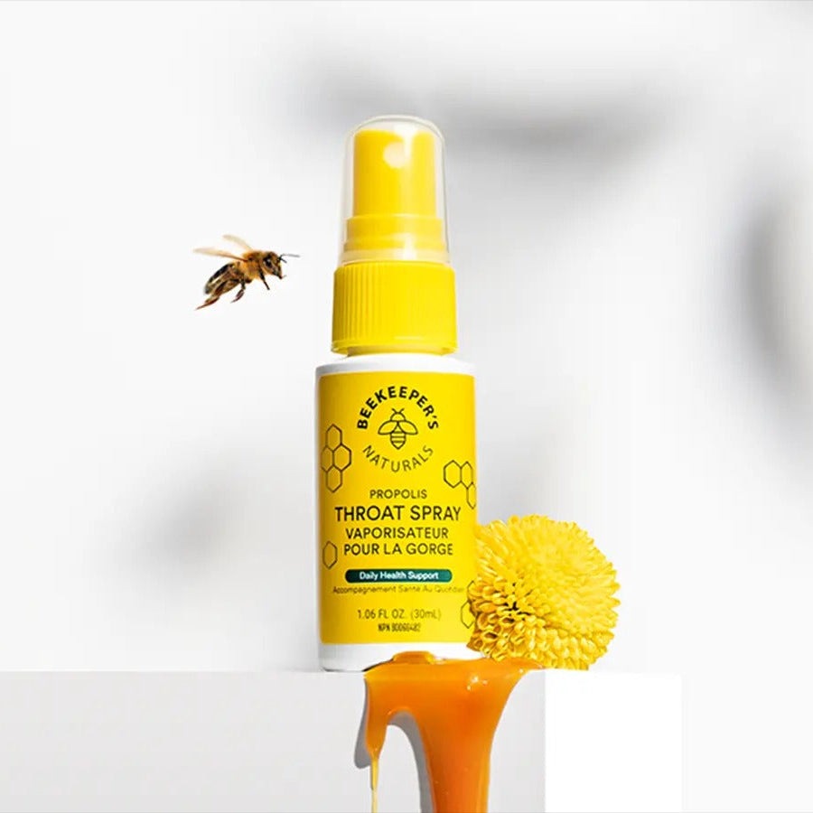 Beekeeper's Naturals Propolis Throat Spray 30 ml, yellow spray bottle ready to mist beside honey drip and bee.