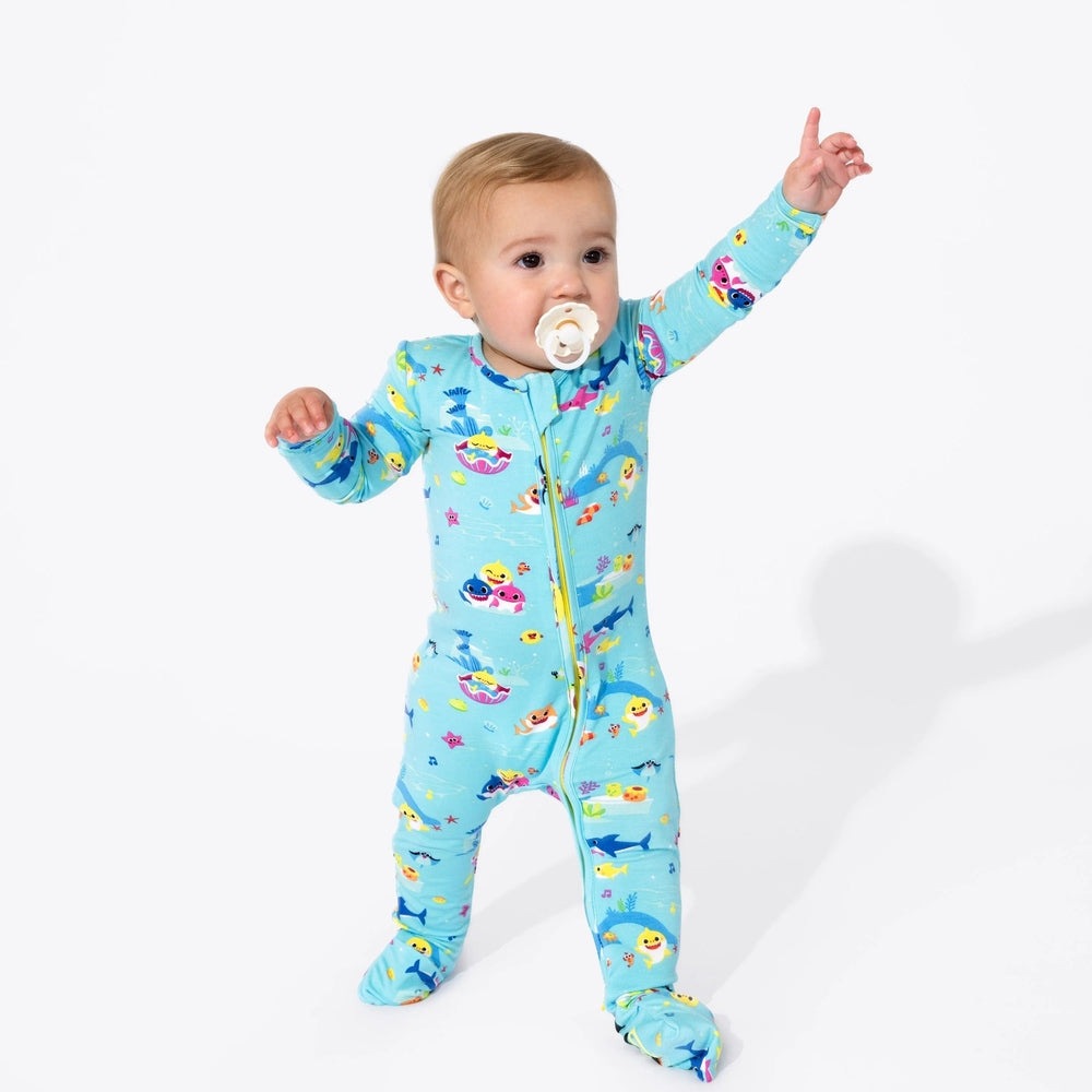 Bellabu Bear Bamboo Convertible Footie Baby Shark in blue; baby stands with arms raised, pacifier in mouth.