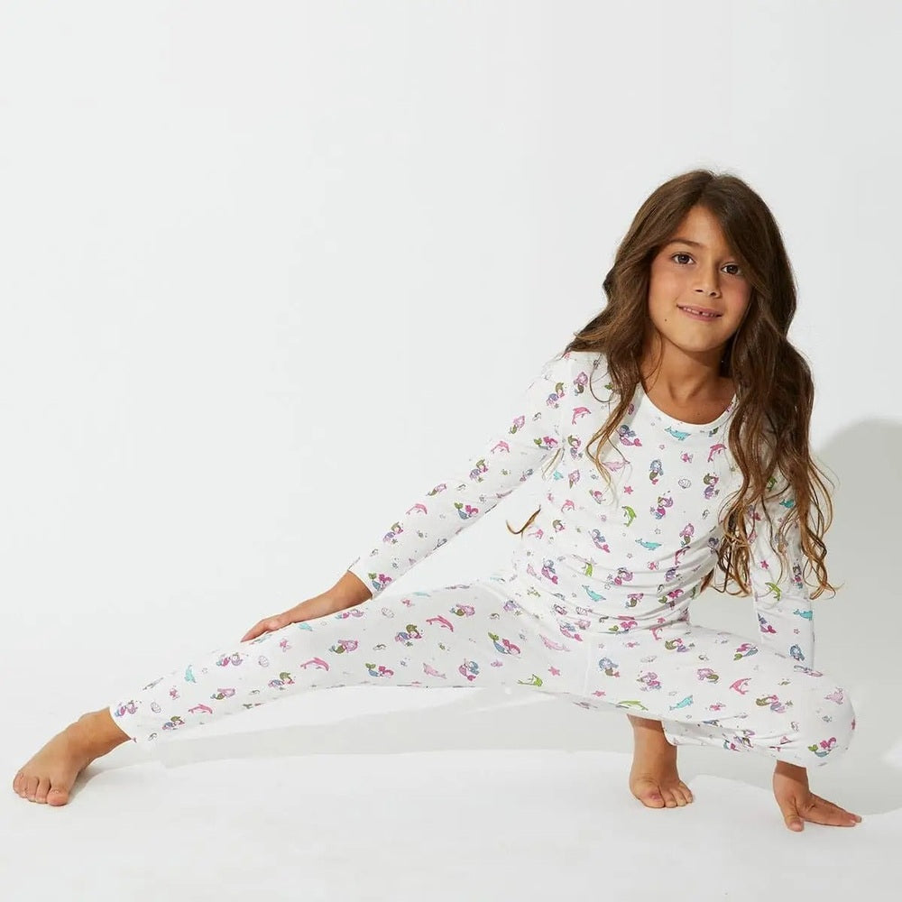 Bellabu Bear Bamboo Kids Pajamas Mermaid set in white with colorful mermaids, as a girl stretches in a pose.