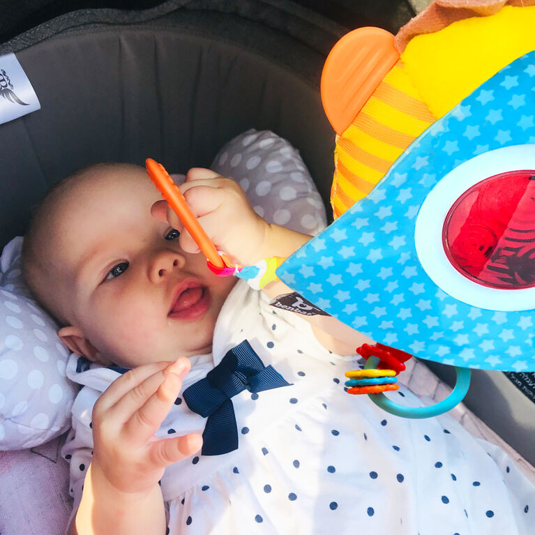 Benbat Travel Toy Lion Power hanging in car seat, blue star-pattern panel with red lens; baby reaching for it.