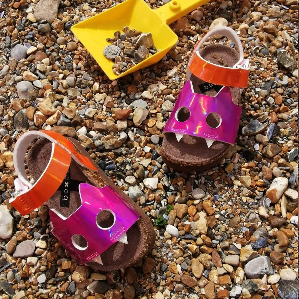 Boxbo Fox Cork Clog Unisex Sandal Fuchsia with orange strap, two pairs resting on a pebble beach.