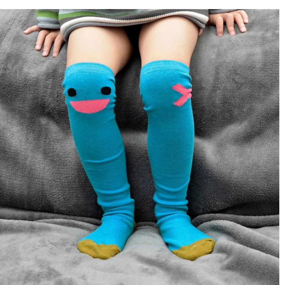 Boxbo Wistiti High Sock Blue knee-highs worn by a toddler, bright blue with pink smile and pink X detail.