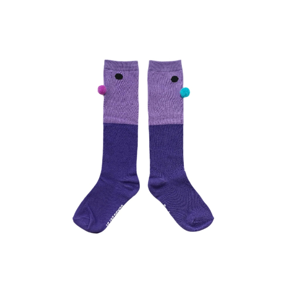 Boxbo Wistiti High Sock Violet pair of purple knee-high baby socks with pink and turquoise pom-poms, laid flat to show color blocks.