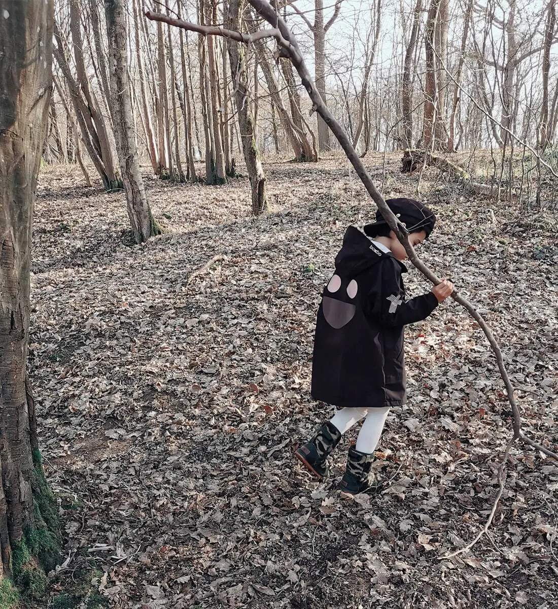 Child wearing a black BOXBO Wistiti rain jacket on a woodland swing