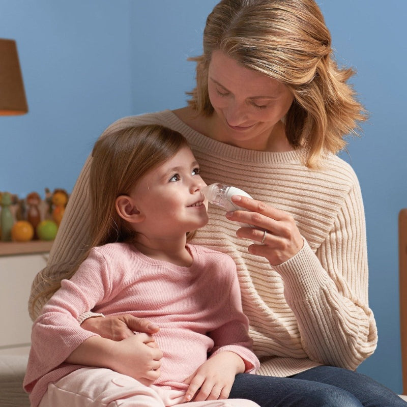 Braun electric nasal aspirator with clear nozzle and white body used by mother on a smiling toddler