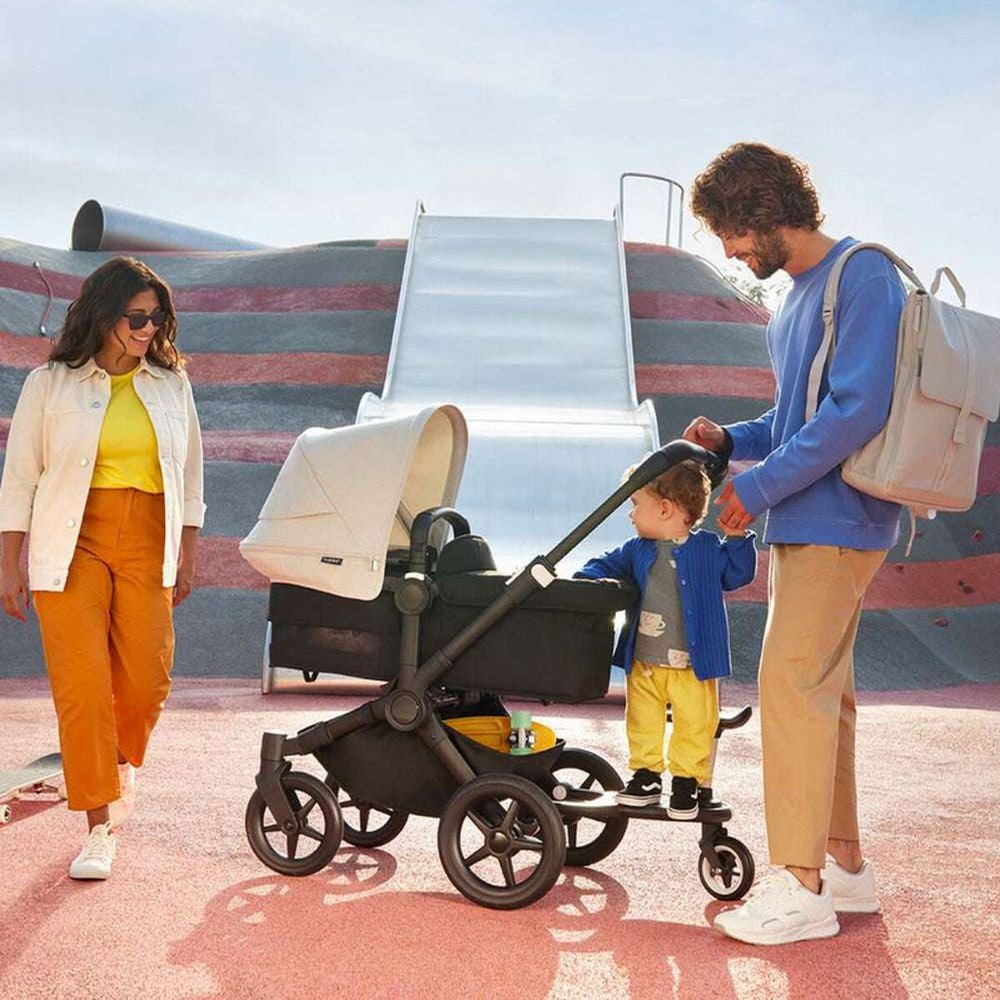 Bugaboo Comfort Wheeled Board+ black stroller accessory for a child on board with a family in the background