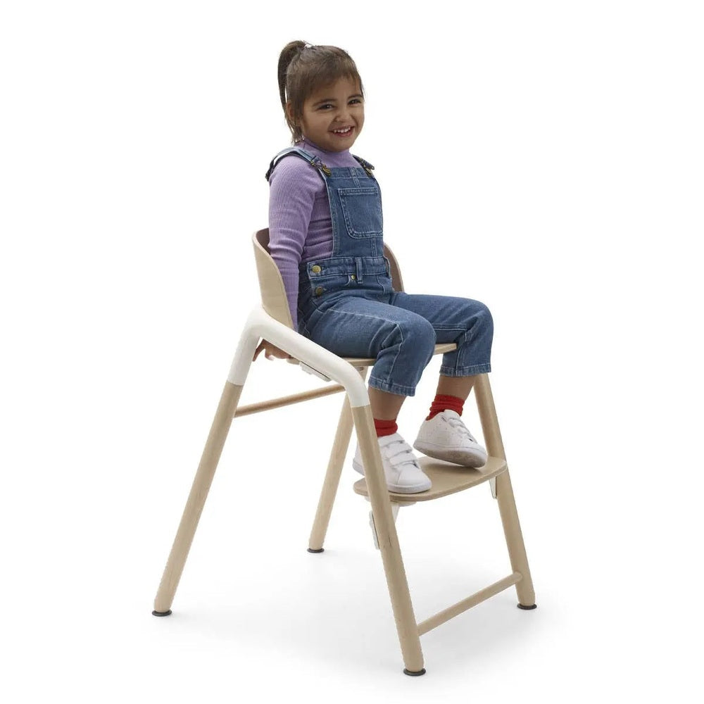 Bugaboo Giraffe Complete High Chair Set in natural wood and white with beige seat, a smiling child sits securely in it.