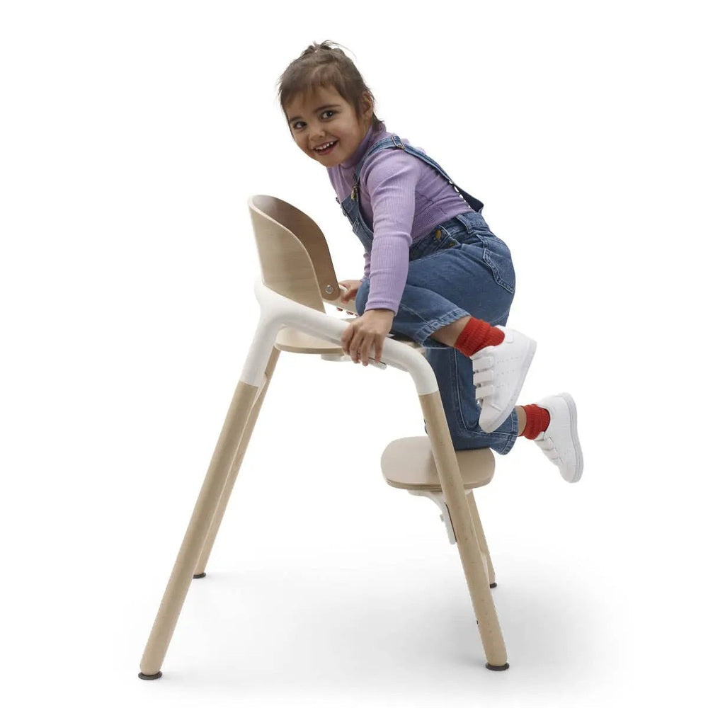 Bugaboo Giraffe Complete High Chair Set in white seat, natural wood legs; child climbs it.