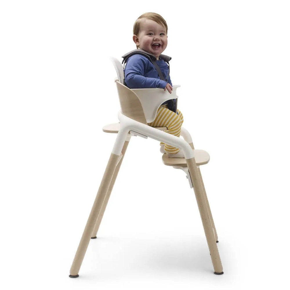 Bugaboo Giraffe Complete High Chair Set, white with natural wood legs, smiling toddler strapped in.