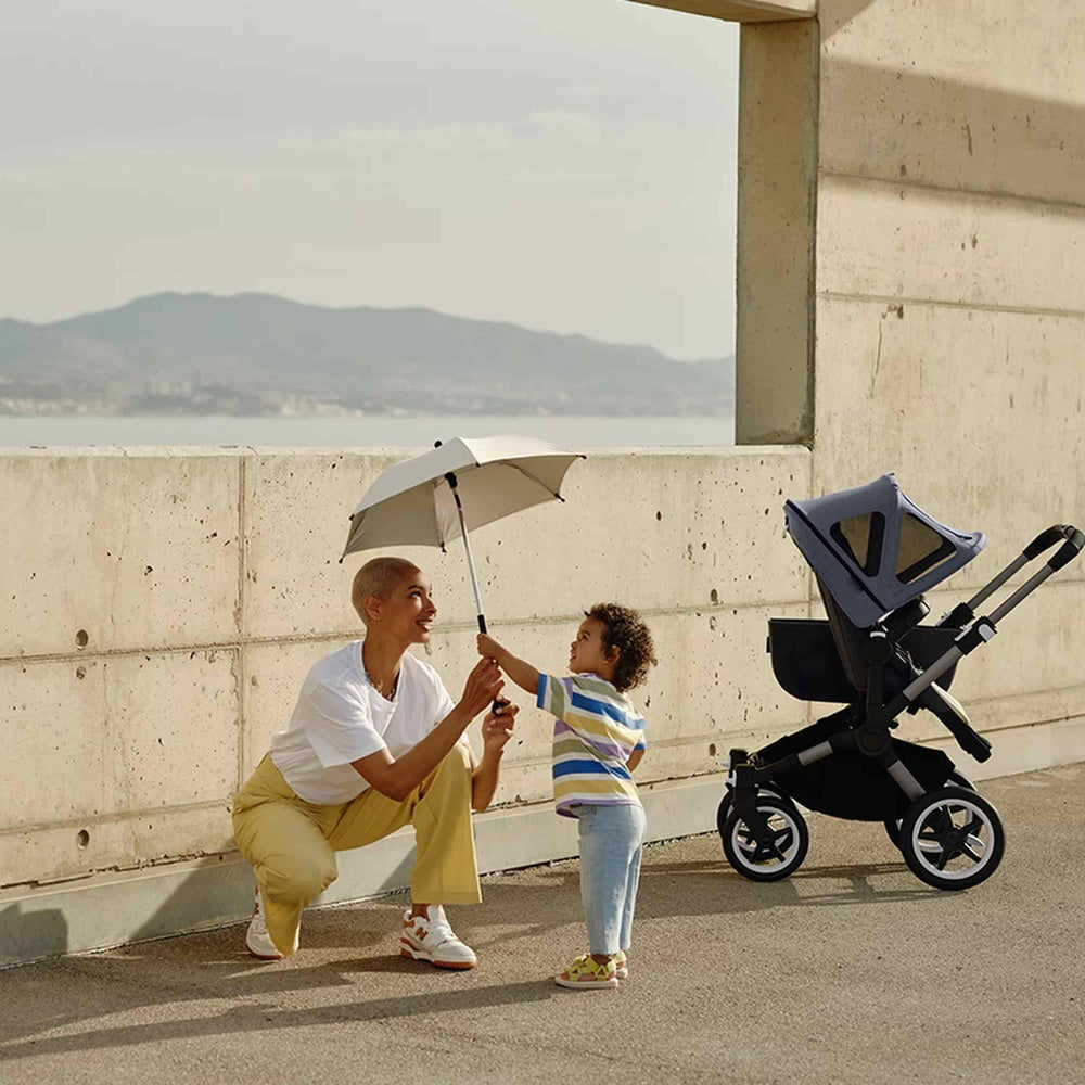 Woman holding an umbrella over a child with a stroller in the background on a rooftop.