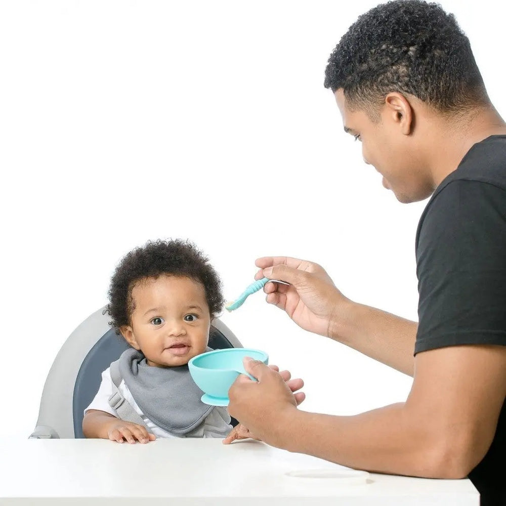 Bumkins Silicone First Feeding Set turquoise bowl and spoon, parent feeding baby at the table.