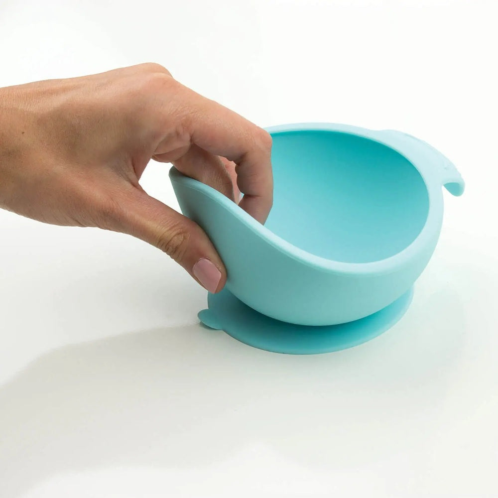 Bumkins Silicone First Feeding Bowl pastel blue with suction base; hand lifts the rim to show secure grip.
