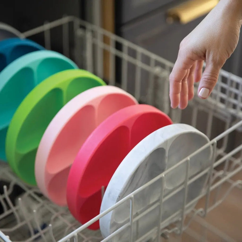 Bumkins Silicone Grip Dish set of six colorful bowls; a hand places them on a dishwasher rack.