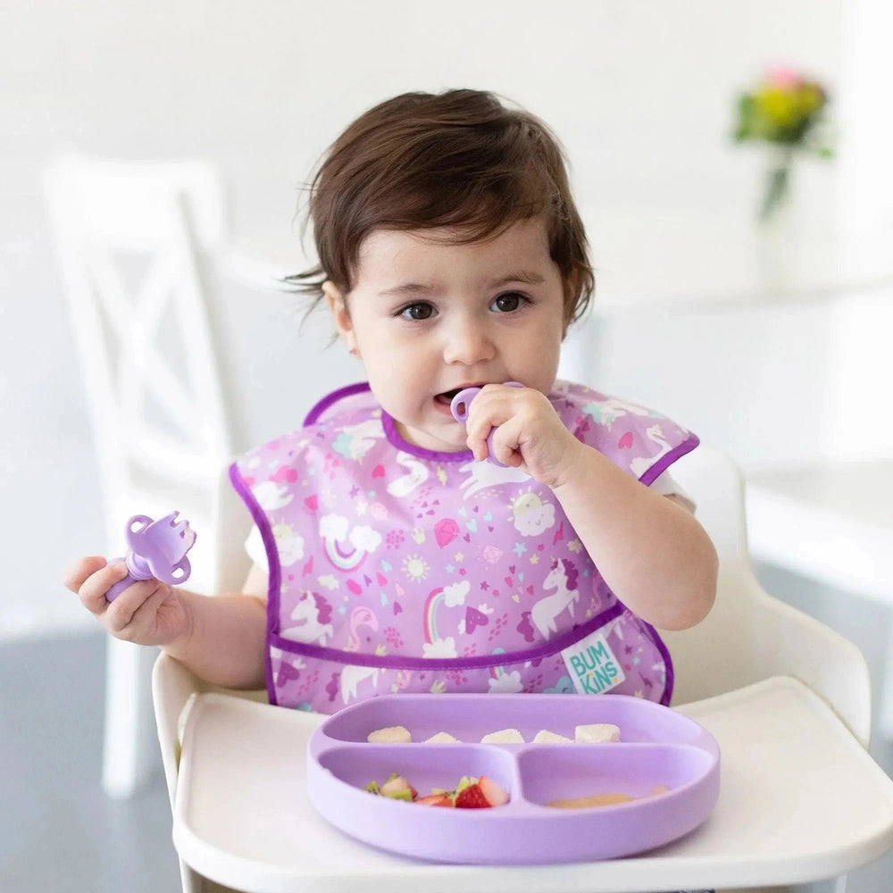 Bumkins Silicone Grip Dish lilac divided plate with suction base shown on a high chair tray as baby eats fruit.