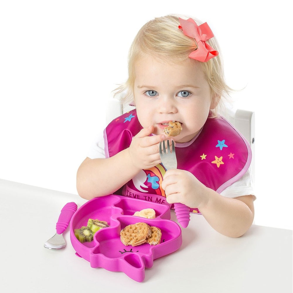 Bumkins Silicone Grip Dish Unicorn: pink unicorn-shaped silicone plate with compartments, toddler feeding with a spoon.