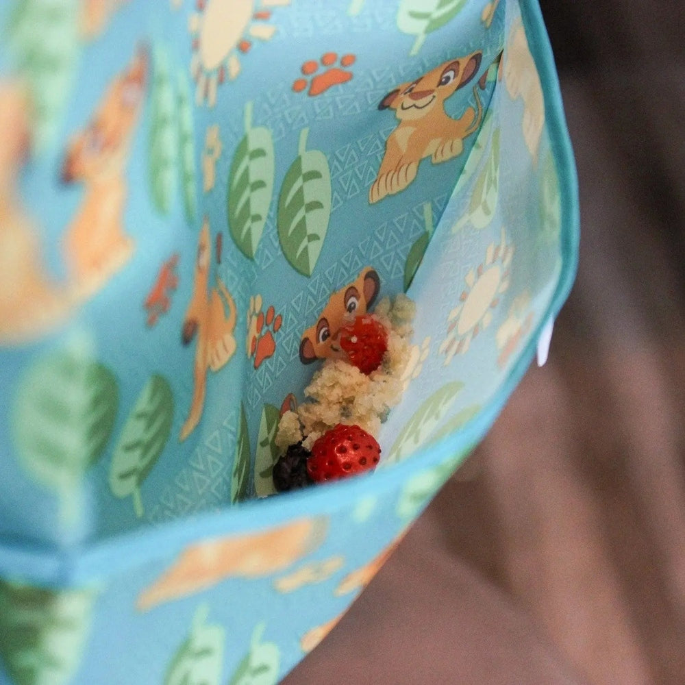BUMKINS Sleeved Bib in blue animal print with crumb-catching pocket catching crumbs during mealtime.