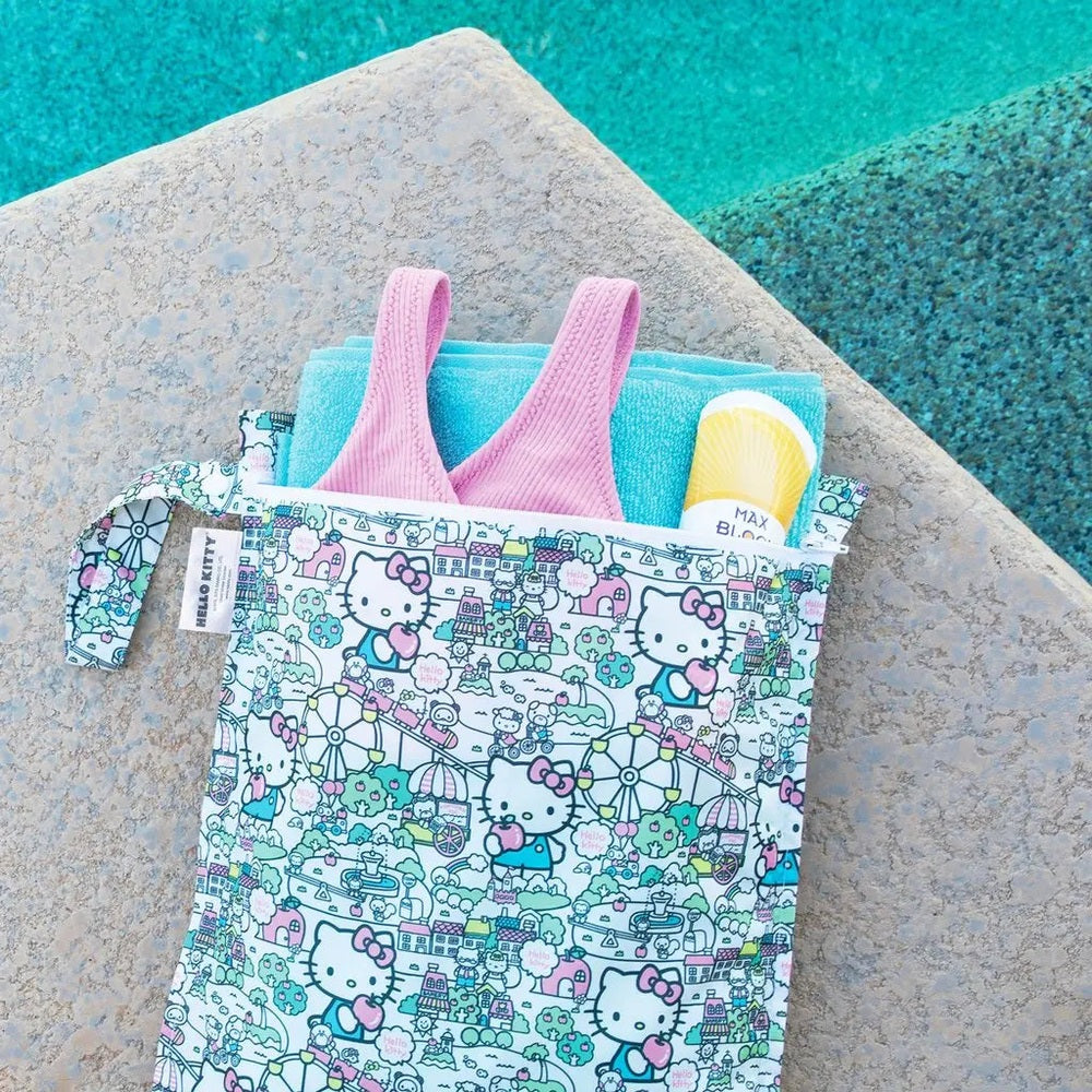 BUMKINS Wet Bag Hello Kitty print with pink handles, opened to reveal a blue towel and sunscreen inside.