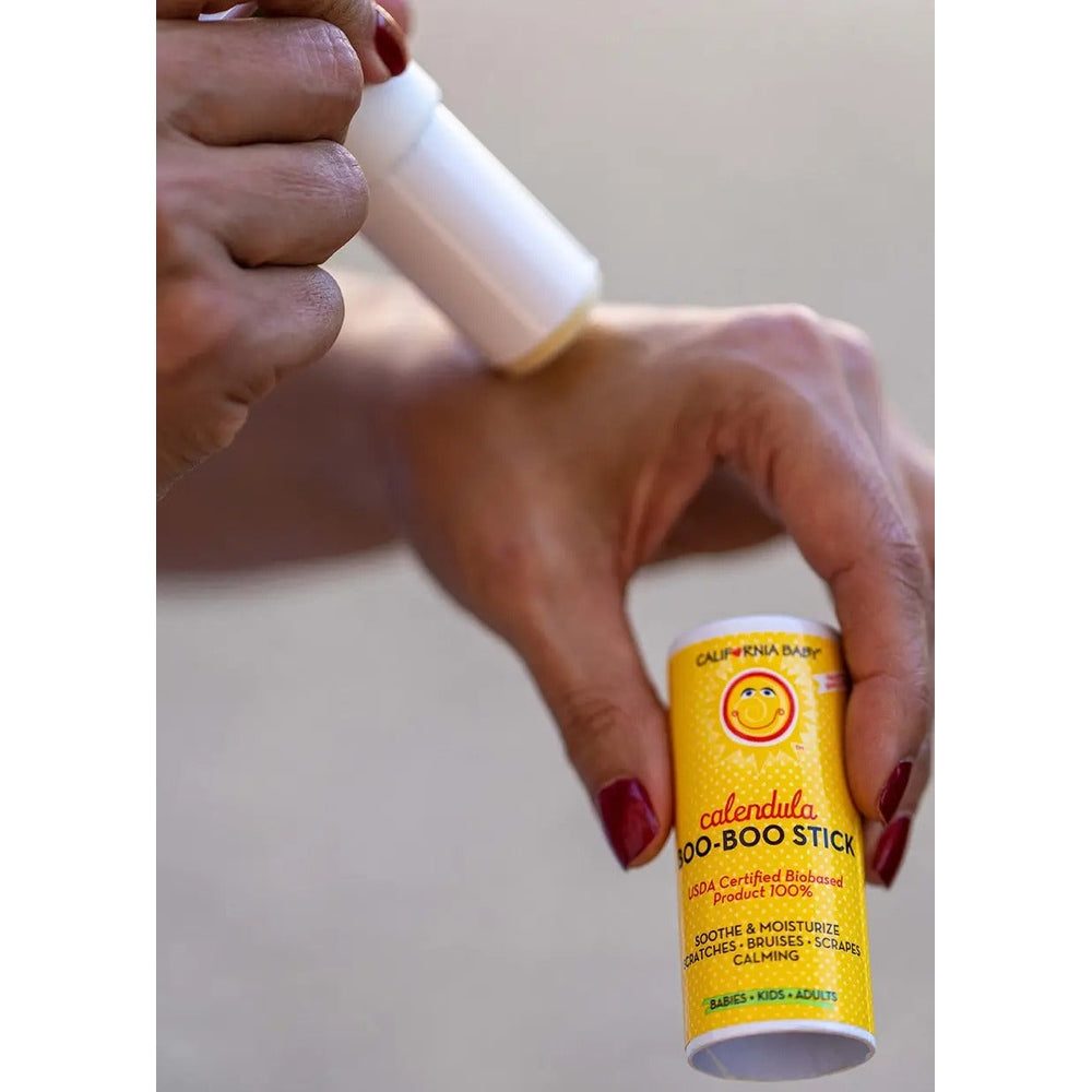 California Baby Boo-Boo Stick in yellow label; white tube with white cap being applied to skin