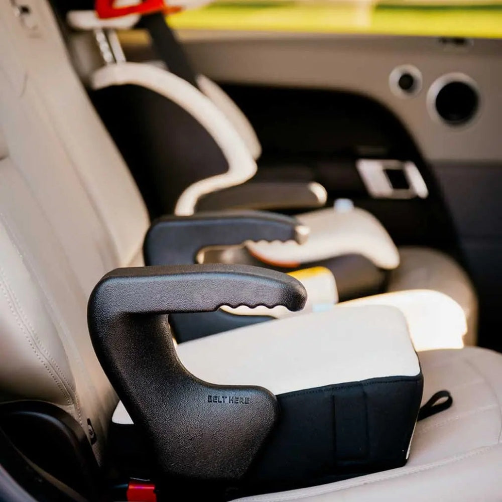 Clek Booster Seat Olli in black/gray sits on a car seat, belt guides visible for secure fit.