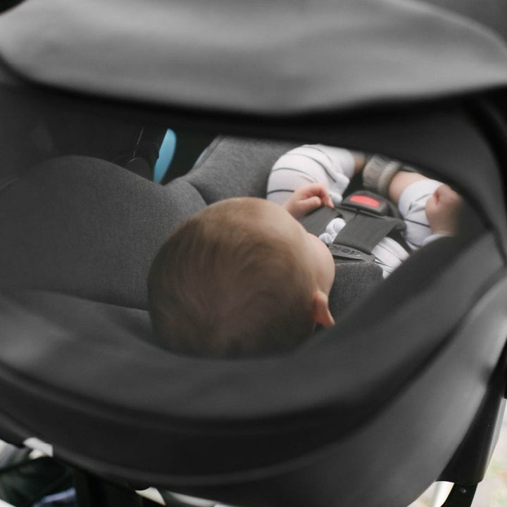Clek Liingo Railroad infant car seat with gray interior and a securely strapped baby.