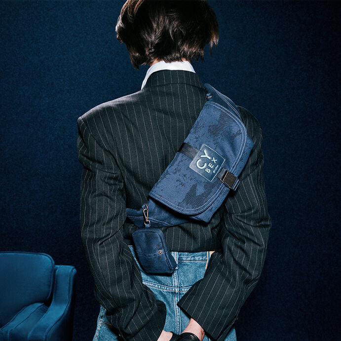 Close-up of the Cybex Belt Bag Rebellious Luxury Denim Blue denim blue cybex belt bag with distressed patch pattern worn crossbody at back, features buckle strap and small front pouch.