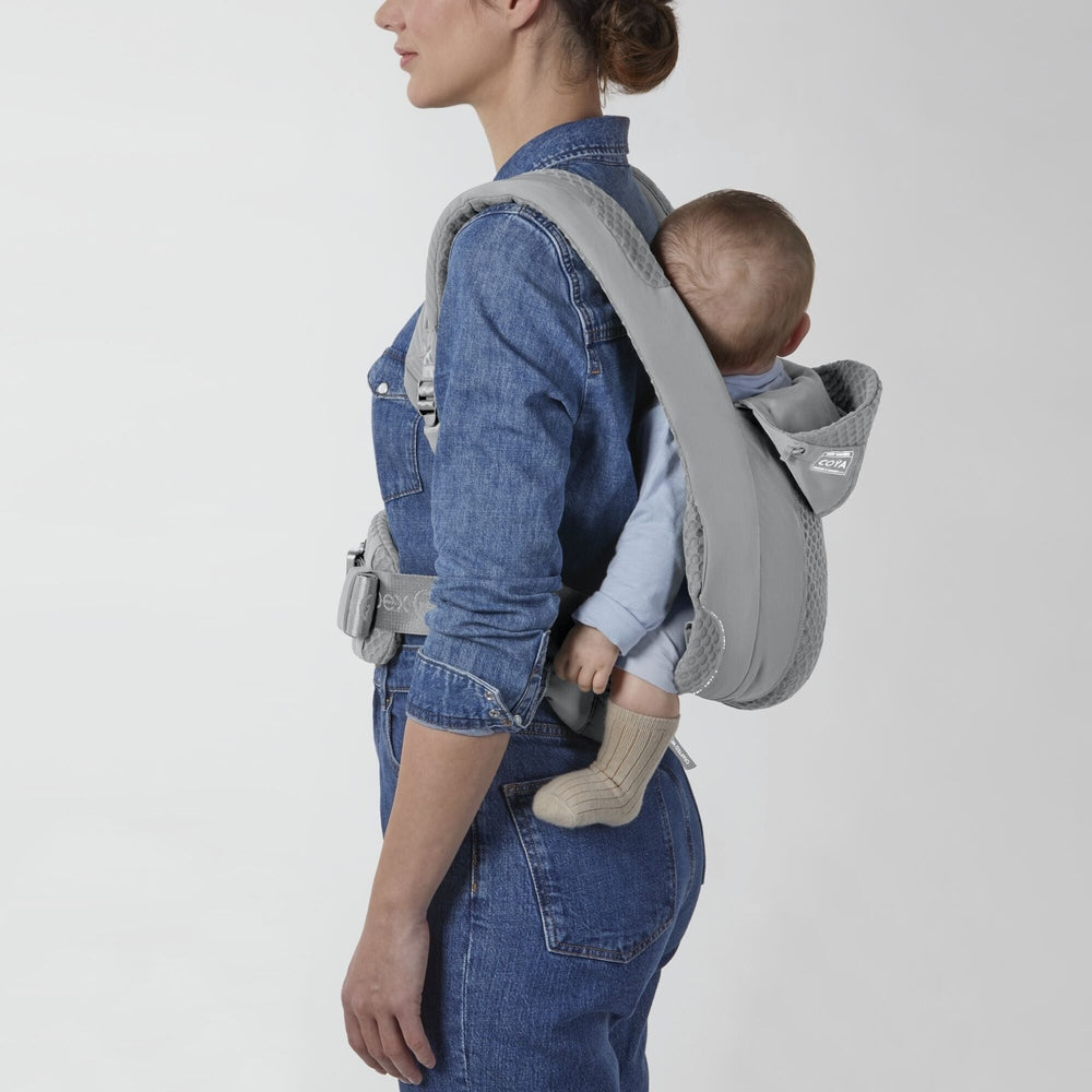 Close-up of the Cybex Coya Carrier grey cybex coya baby carrier with padded straps and waist belt; baby in light-blue outfit on denim-clad parent.
