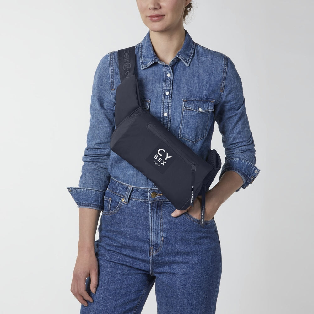 Close-up of the Cybex Coya Carrier in dark navy nylon, worn diagonally across chest with crossbody strap and front logo.