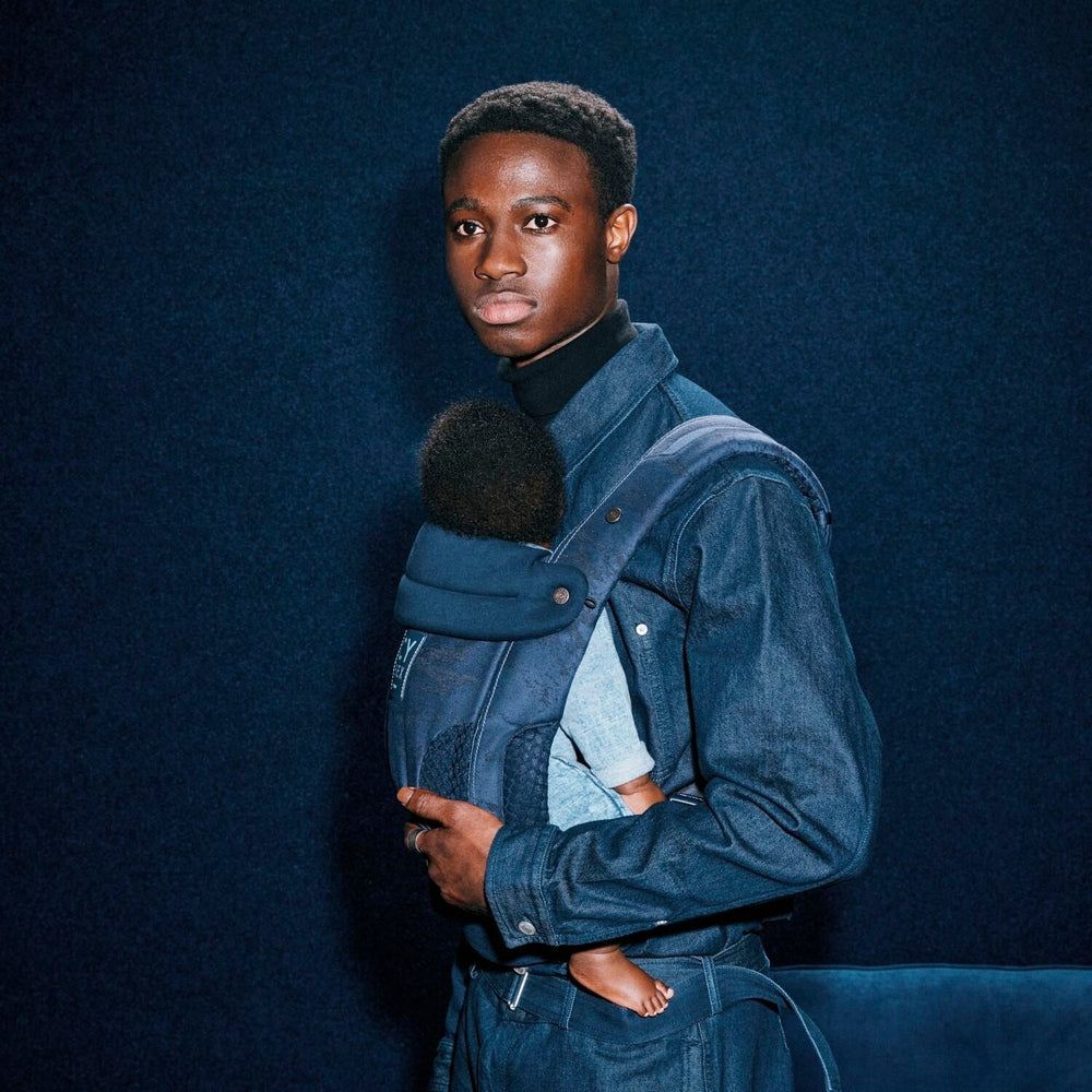 Close-up of the Cybex Coya Carrier Rebellious Luxury Denim Blue denim blue cybex coya baby carrier worn by man, baby snug inside with plush fur-trim hood.