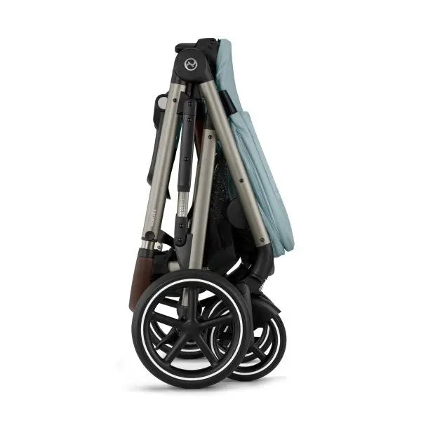 Close-up of the Cybex Gazelle S V2 Stroller folded for compact storage, blue fabric, silver frame, black wheels.