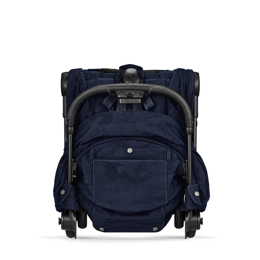 Close-up of the Cybex Platinum Coya Compact Lightweight Stroller - Rebellious Luxury Denim Blue folded cybex coya compact stroller in rebellious denim blue fabric, with black padded handlebar and front pocket detail.