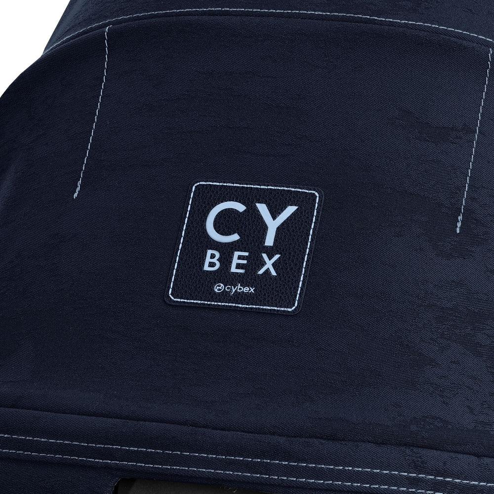 Close-up of the Cybex Platinum Priam 4 Stroller Limited Edition - Rebellious Luxury Denim Blue denim-blue priam 4 stroller fabric with light blue stitching and a square cybex logo patch.