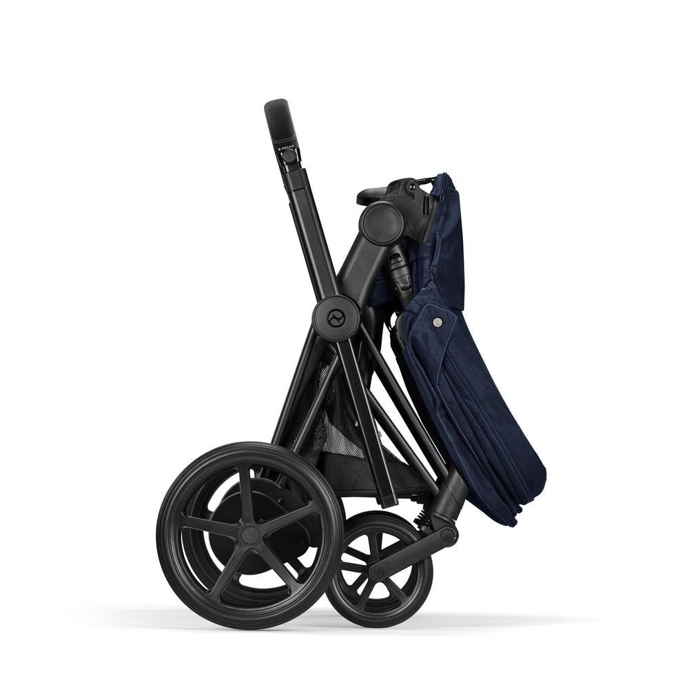 Close-up of the Cybex Platinum Priam 4 Stroller Limited Edition - Rebellious Luxury Denim Blue in denim blue fabric, black frame, folded with large rear wheels.