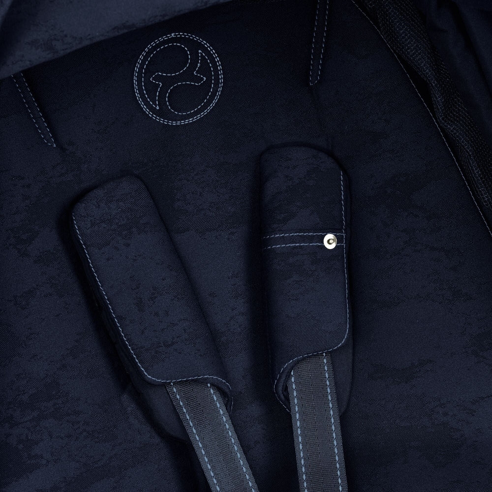 Close-up of the Cybex Platinum Priam 4 Stroller Limited Edition - Rebellious Luxury Denim Blue navy denim-pattern stroller fabric with light blue contrast stitching, padded straps, and circular logo patch.