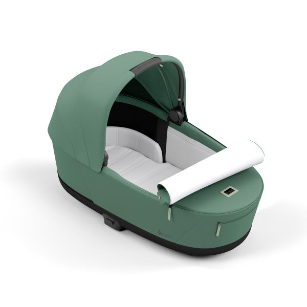 Close-up of the Cybex Platinum Priam Lux Carry Cot in green with white interior, sun canopy, and carry handle.