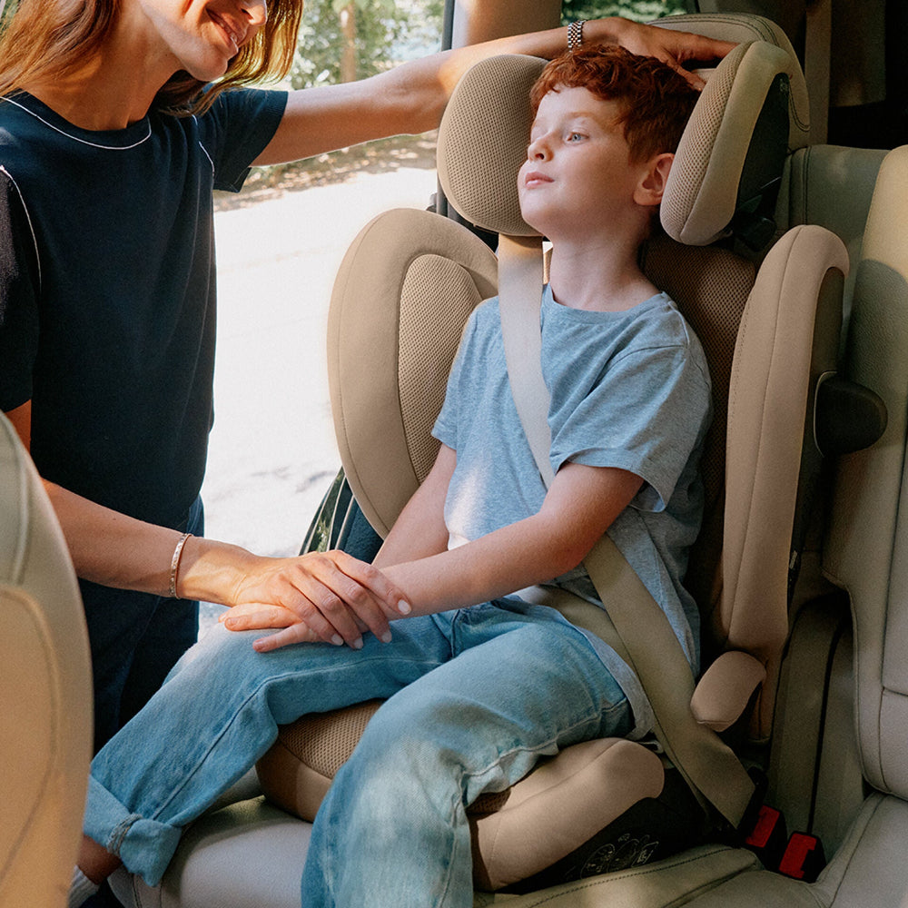 Close-up of the Cybex Solution G2 Booster Seat with beige interior; child buckled in blue t-shirt sits beside an adult.