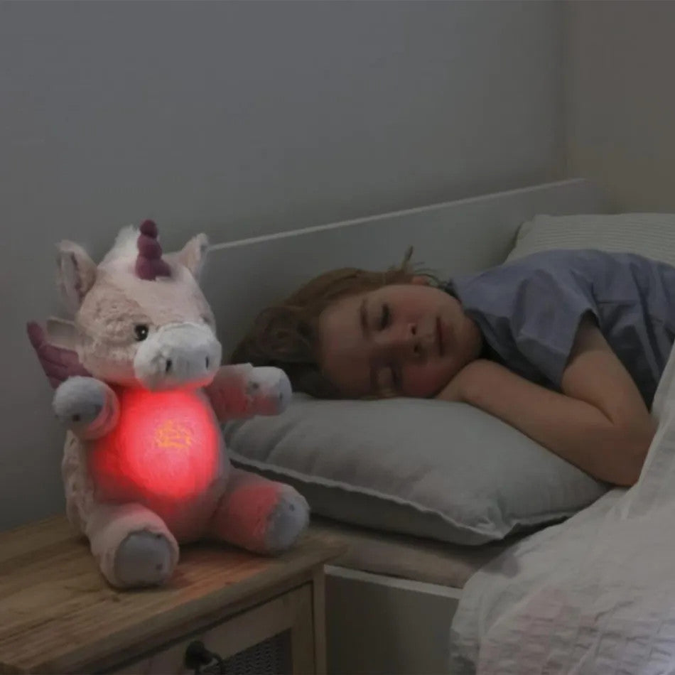 Cloud B Love Light Lily the Unicorn plush with glowing red heart beside a child in bed