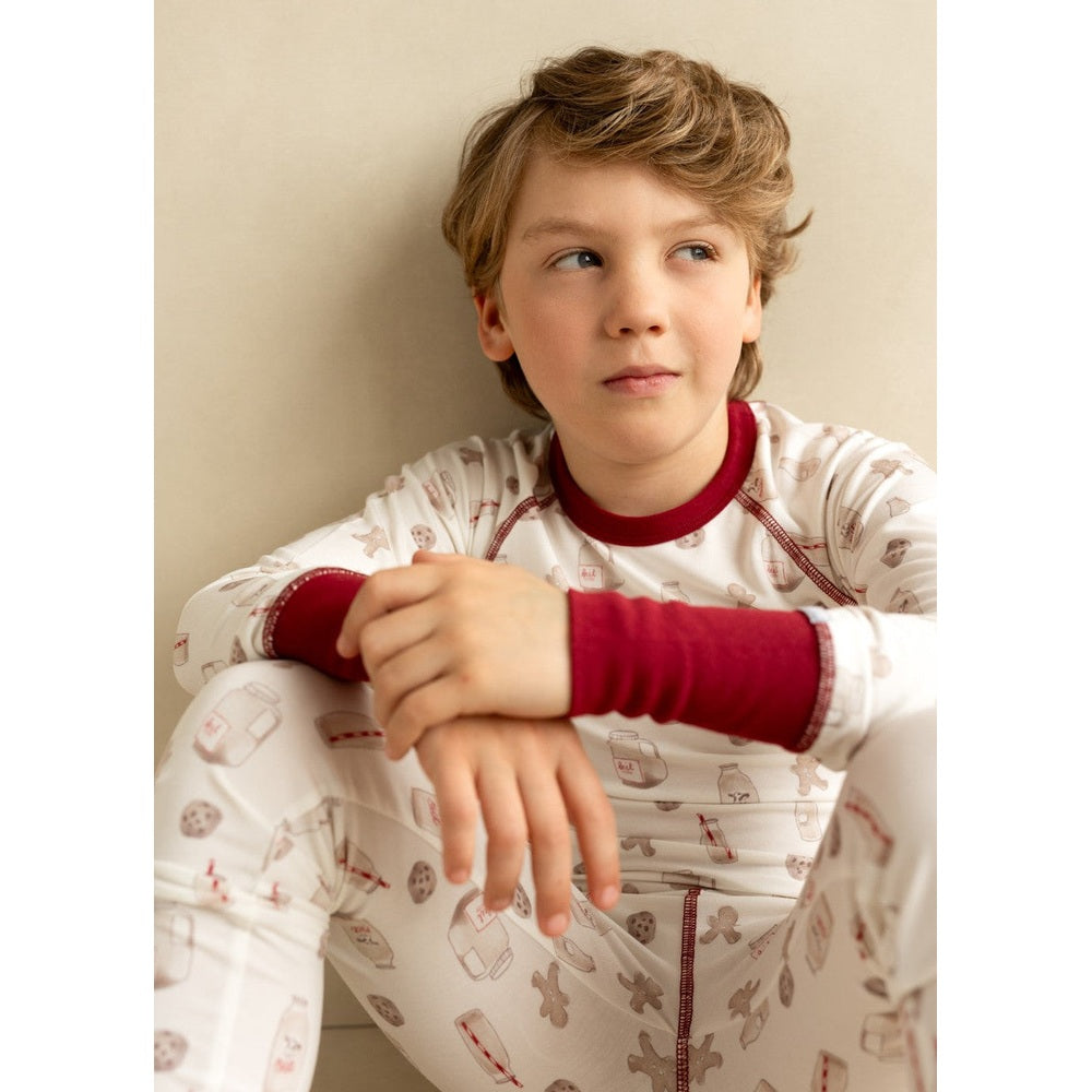 Coccoli Kid Long Sleeved Cotton TENCELTM Modal Pyjama Cookies On Cream; a boy sits cross-legged in cream pajamas with red cuffs.