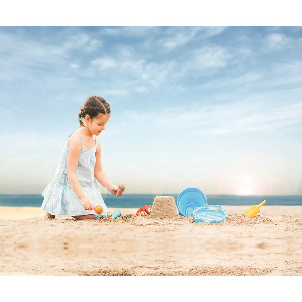Child playing on a sandy beach with sand toys and a blue sky.