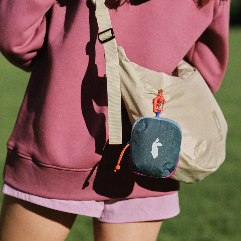 Cotopaxi Allpita Mini Bag in Teal with orange zipper pull, attached to a beige crossbody bag.