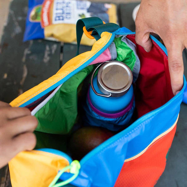 Cotopaxi Taal Convertible Tote in blue exterior with orange panels and red interior, open with water bottle inside.