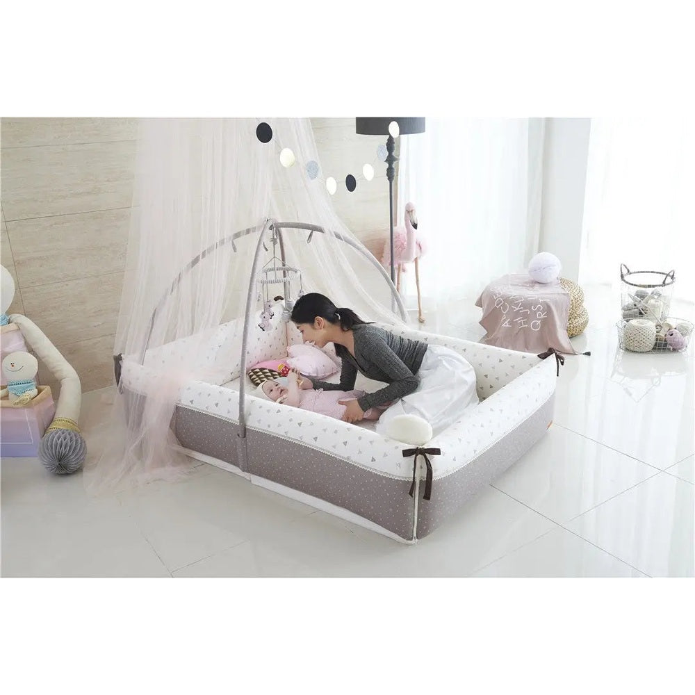 Creamhaus Inua bumper bed canopy in grey and white; mother leans over baby inside the breathable mesh canopy.