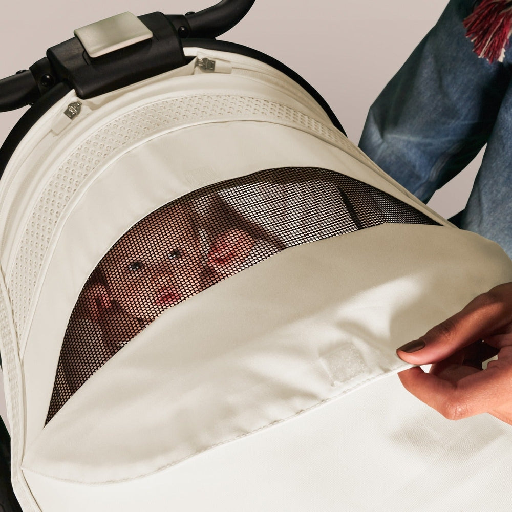 Close-up of the Cybex Avi Spin All Terrain Stroller with white fabric and mesh peek window, parent adjusting the canopy.