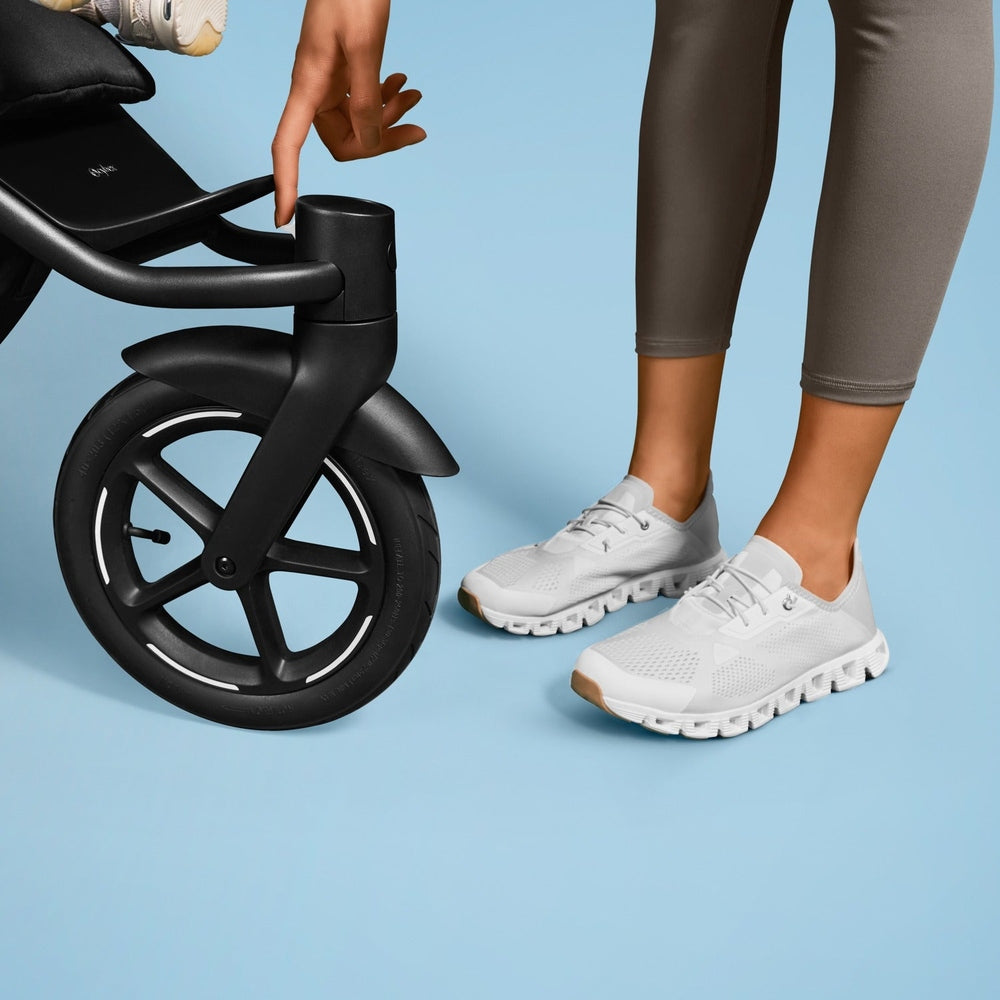 Close-up of the Cybex Avi Spin All Terrain Stroller in black, parent adjusting the front handle near the large wheel.