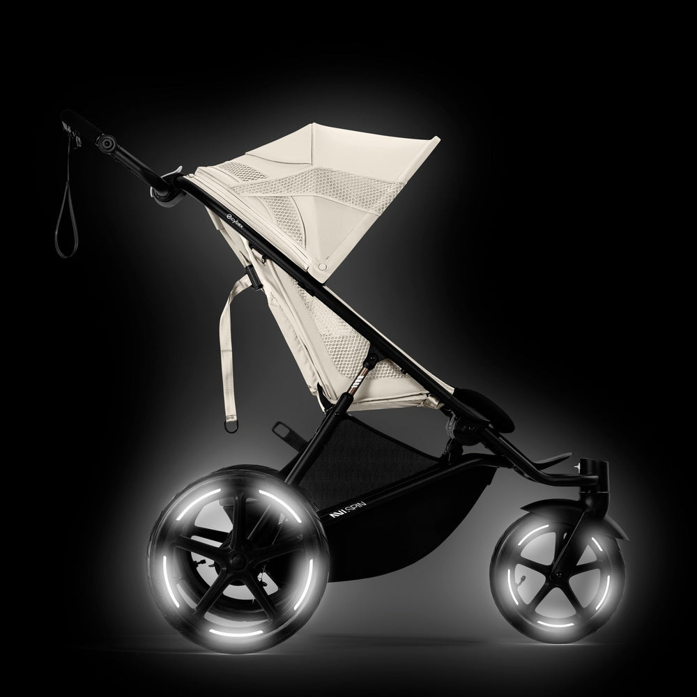 Close-up of the Cybex Avi Spin All Terrain Stroller in cream seat on a black frame, ready to roll with illuminated wheels.