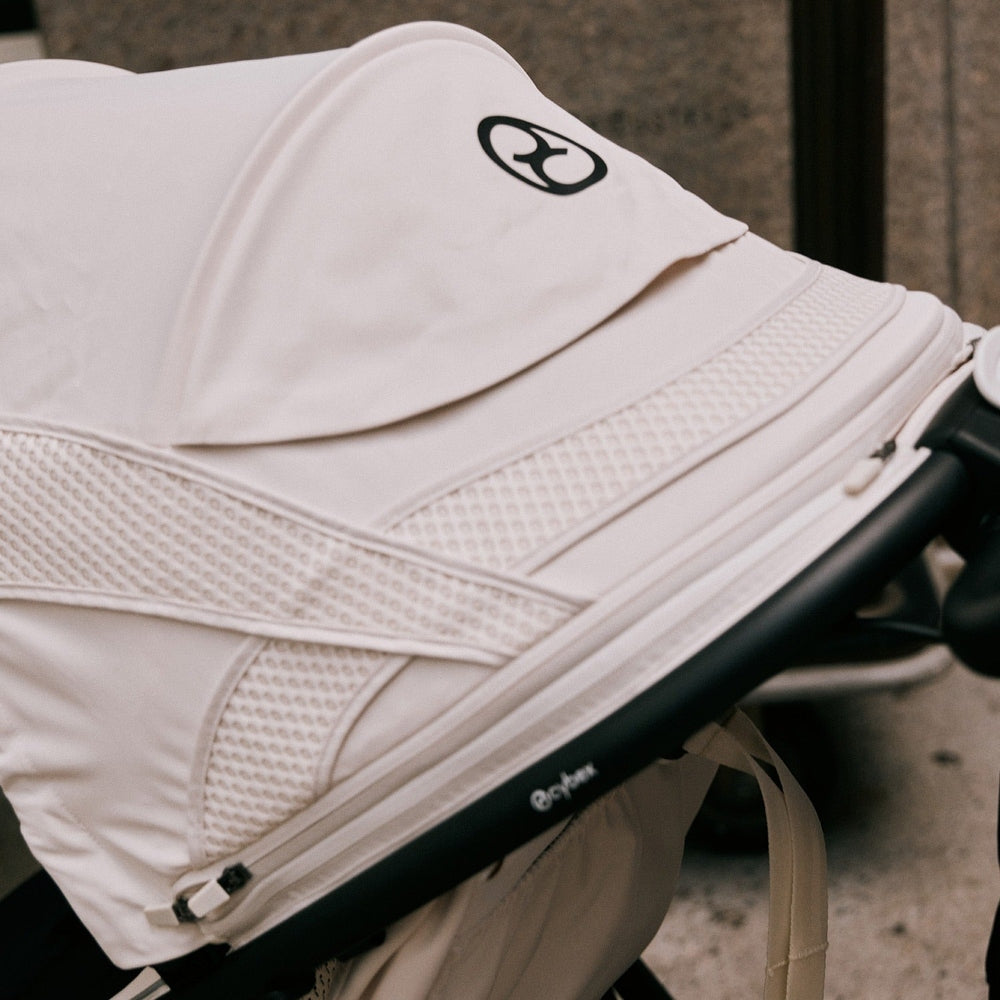 Close-up of the Cybex Avi Spin All Terrain Stroller in white with mesh panels being pushed along a sidewalk.