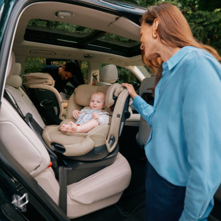 Cybex Callisto G 360 Rotating All-In-One Convertible Car Seat in Almond Beige installed rear-facing in an SUV with caregiver and baby