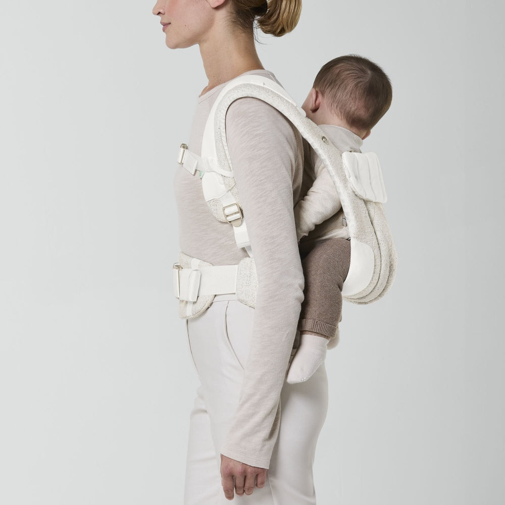 Close-up of the Cybex Coya Carrier Boucle e in cream boucle with padded white straps and waist belt, infant on back.